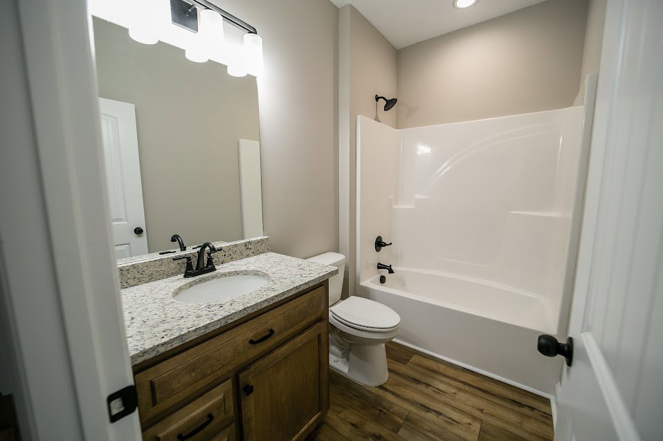 Bathroom with white tile walls, a white bathtub beside a closed-lid toilet, and a rectangular sink featuring a black faucet.