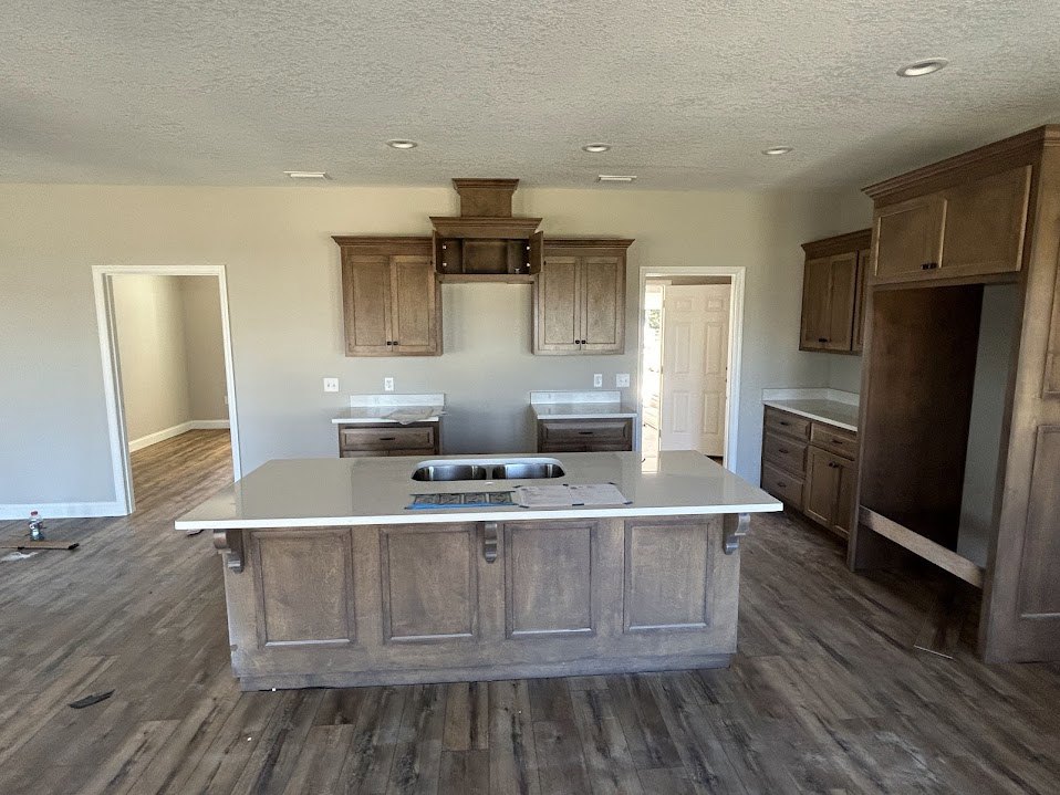 Spacious kitchen featuring a large island with white countertop, integrated sink, white cabinetry with black handles, and open door leading to adjacent room