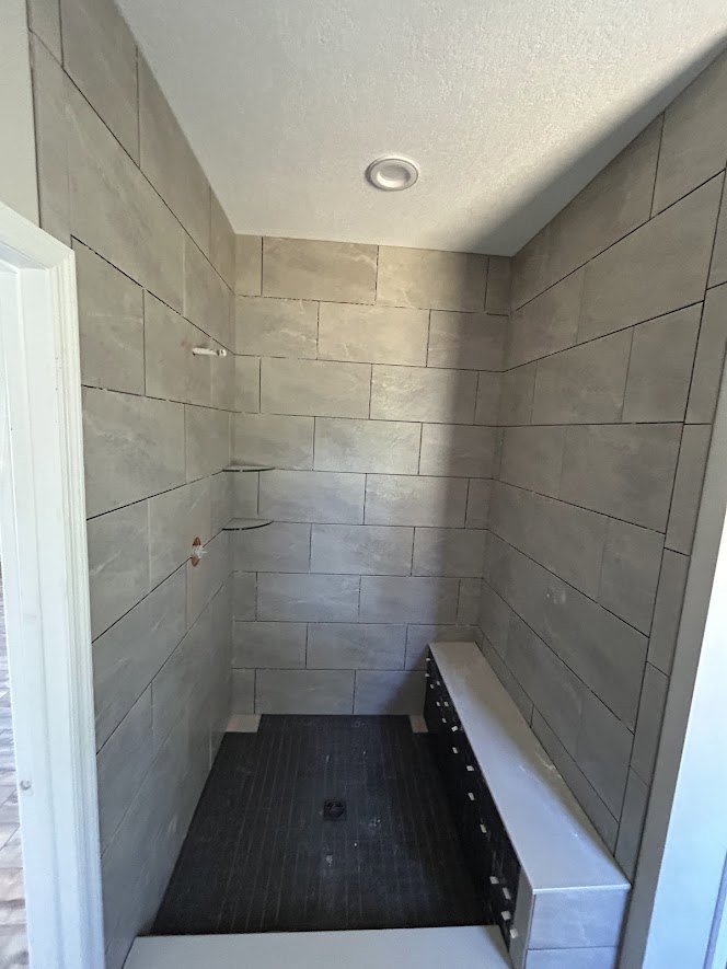Shower with built-in bench and black drawers, tile floor, white door, white ceiling with recessed light