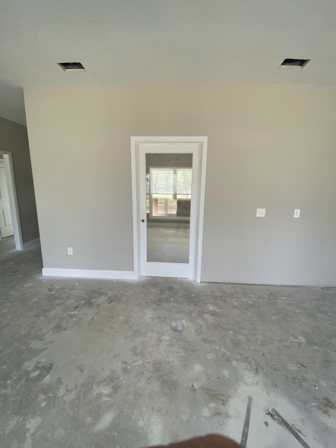 White plaster walls and ceiling, concrete floor, white door with glass window, black trim along baseboard