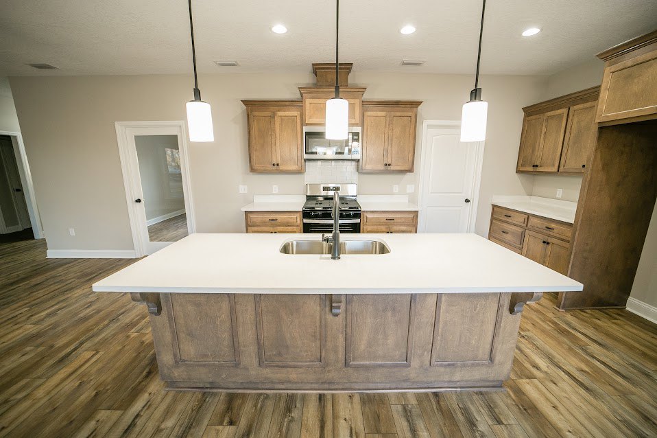 Spacious kitchen featuring a large white island with built-in sink and faucet, surrounding cabinetry, light countertops, and wood flooring