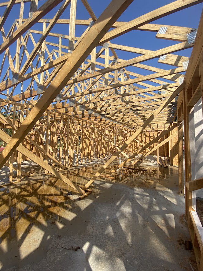 Wood-framed house under construction with exposed beams and concrete foundation, open to the sky.