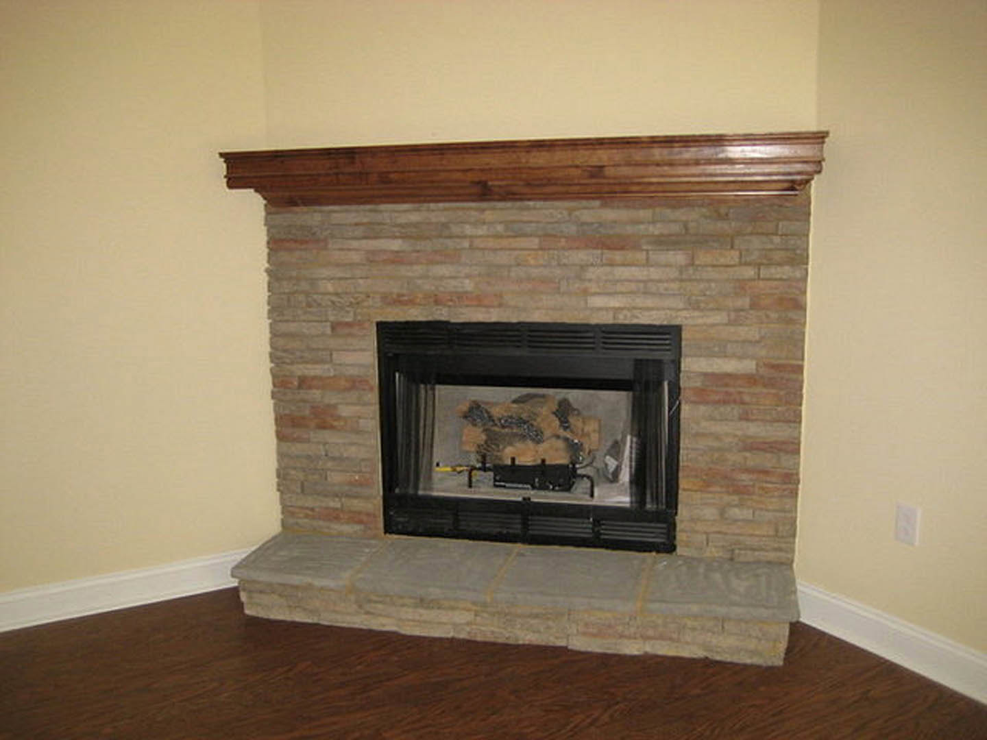Stone fireplace with black-framed glass door, brick hearth, and white mantel shelf in a room with stone flooring and neutral walls