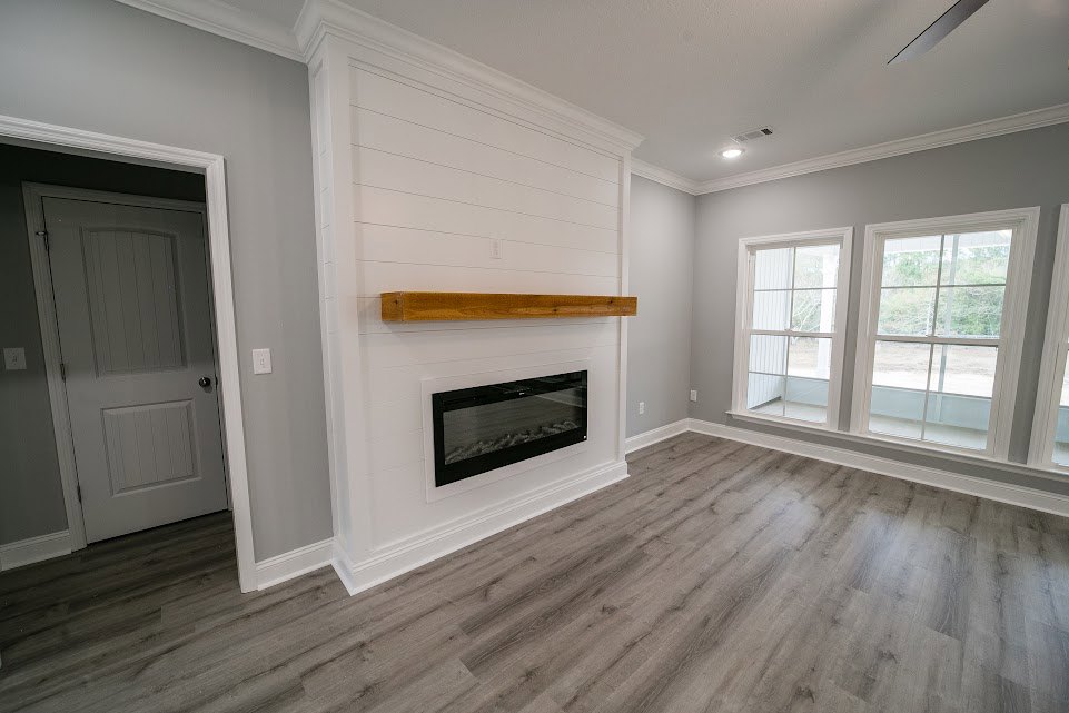 Living room with wood flooring, white-framed window, plaster walls, built-in fireplace, and white door with silver knob