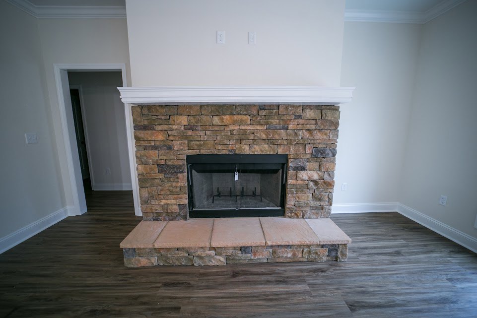 Stone fireplace with wire mesh screen set in a brick accent wall, adjacent to a doorway, stone flooring transitioning to wood floor in a spacious living room.