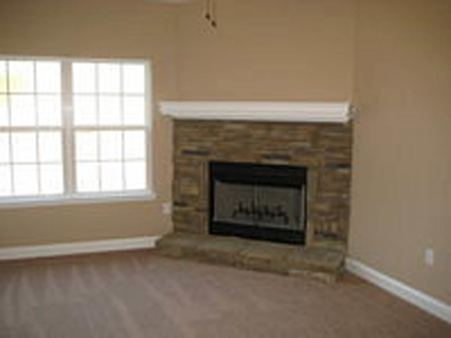 Stone fireplace with textured stone wall, multi-pane window, close-up of stone flooring, wood burning stove, and a blurry black-bordered picture frame in a den.