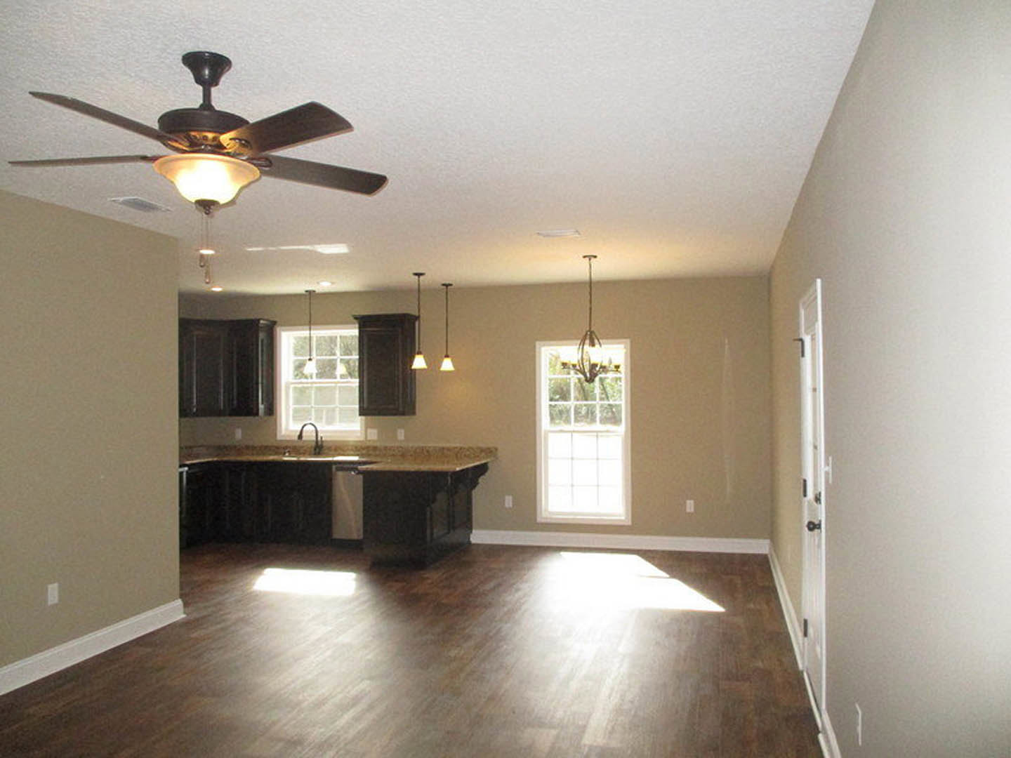 Open-concept kitchen and living room featuring a ceiling fan with light, white-framed window, hardwood flooring, black door, and kitchen countertop with sink