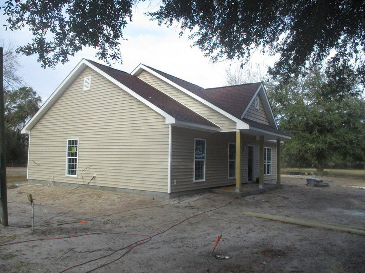 Partially built house with exposed wooden framing, white-framed windows, and a shingled roof, surrounded by dirt lot and scattered construction materials