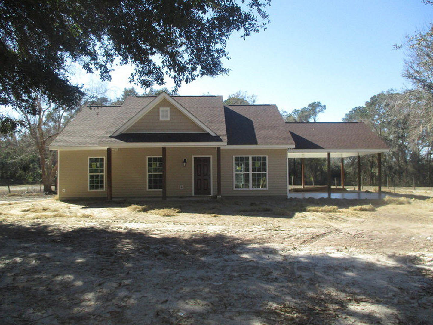 White siding house with covered front porch, square window panes, single entry door, dirt yard, and mature trees in background