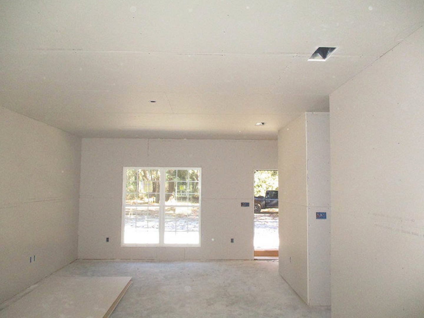 Bright room with white plaster walls, wood door, large window overlooking outdoor greenery, recessed ceiling light, and light-colored flooring