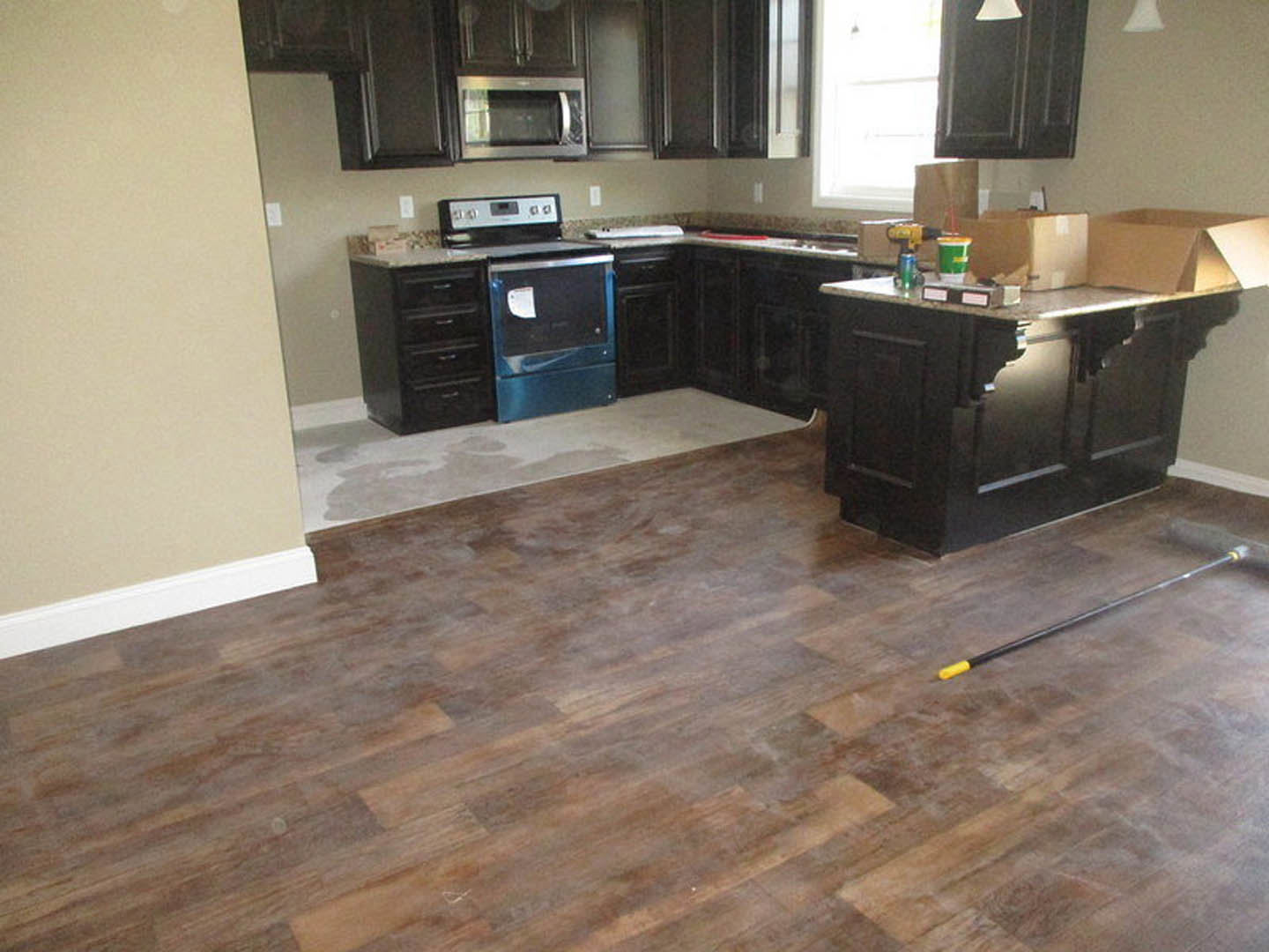 Kitchen with dark wood cabinets, black countertop, stainless steel microwave, wooden flooring, and a stove with a piece of paper on top
