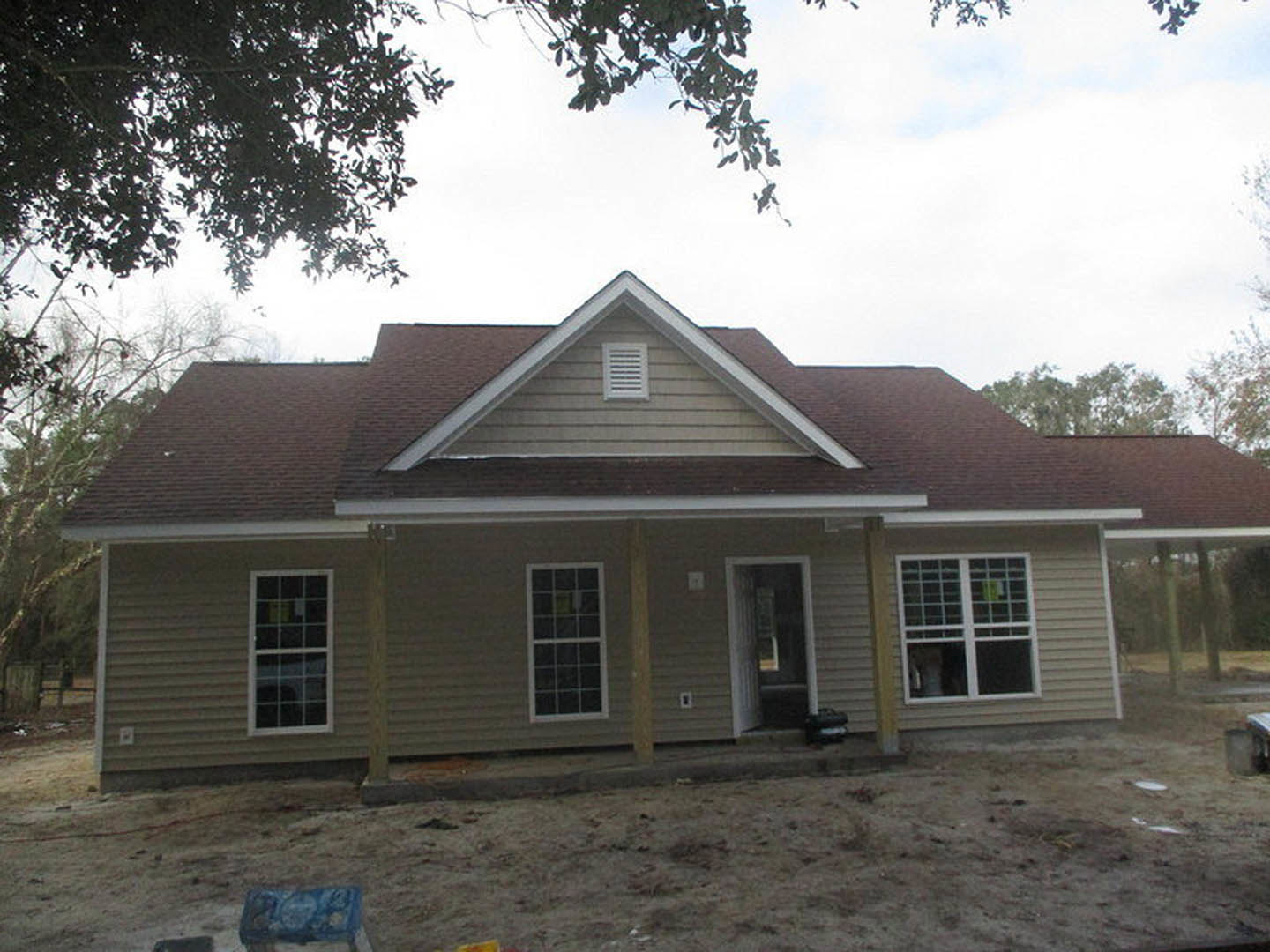 Spacious front porch with white columns, brick exterior walls, multi-pane windows, and gabled roof surrounded by trees
