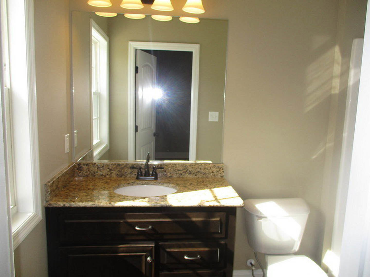 Bathroom with marble countertop sink, white toilet, tile flooring, ceiling lights, and cabinetry with drawers
