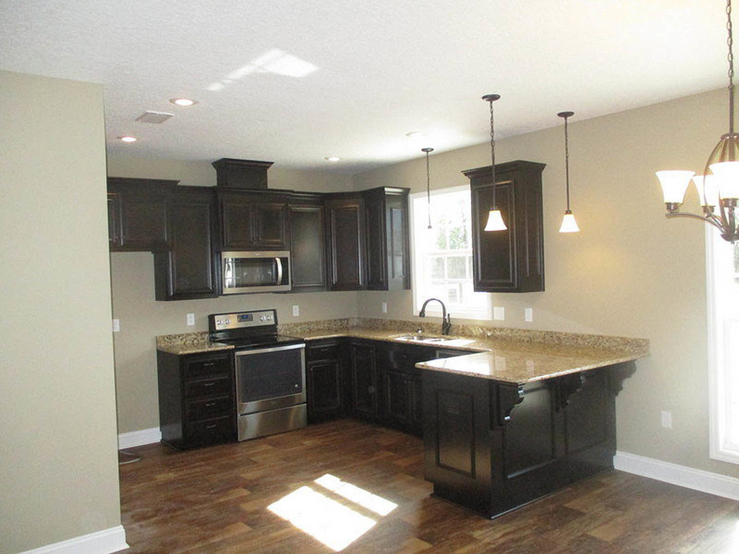 Kitchen with dark wood cabinets, granite countertop, stainless steel microwave, tile backsplash, and pendant light fixture.