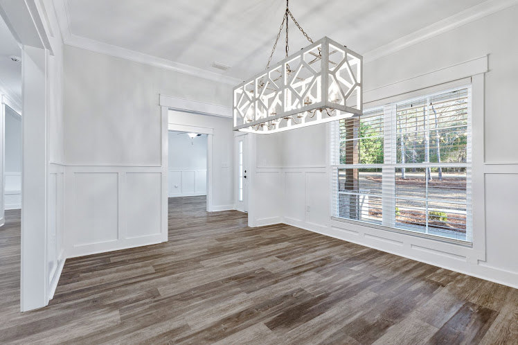 Open room with white rectangular chandelier, hardwood flooring, white walls, and smooth ceiling