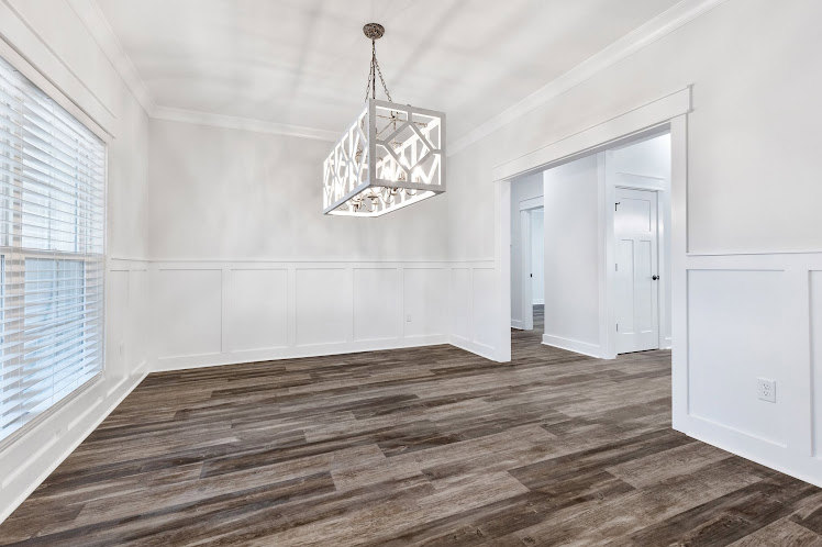 Open-concept living area featuring hardwood floors, neutral walls, and a modern pendant light fixture suspended from the ceiling