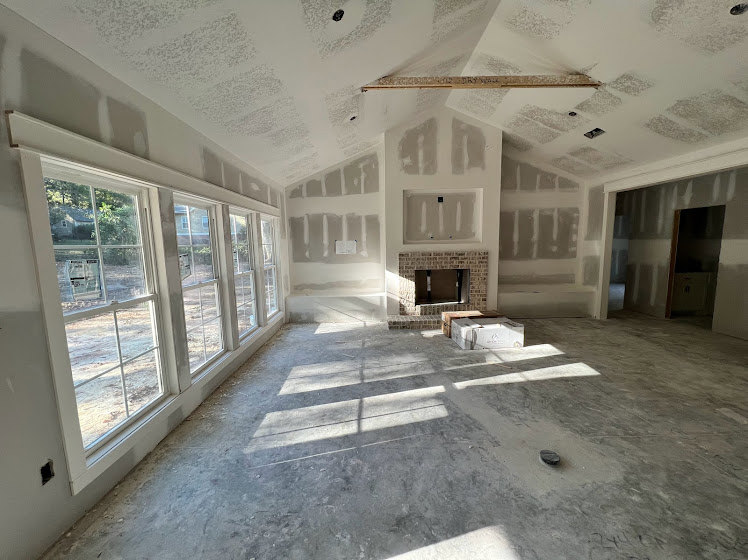 Living room with brick accent wall, large windows, concrete floor, white plaster ceiling, and modern fireplace.