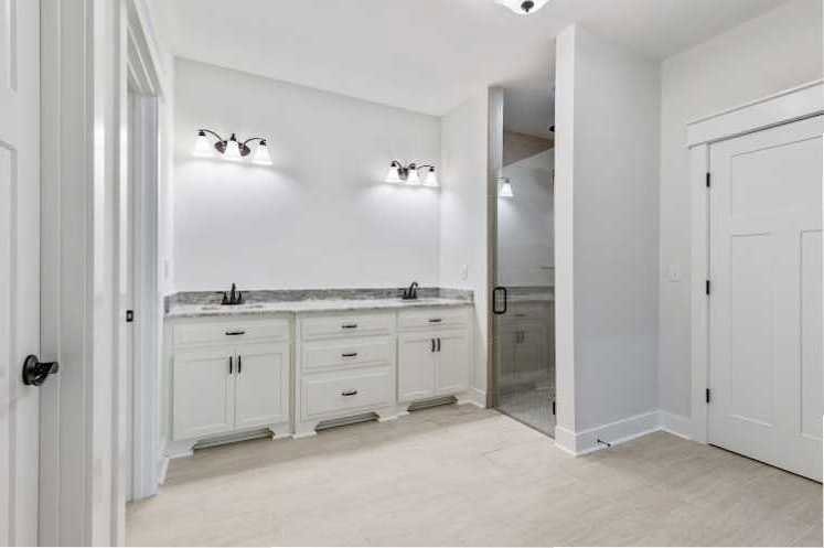 Bathroom featuring white shaker cabinets, glass shower door, white tile flooring, and chrome plumbing fixtures