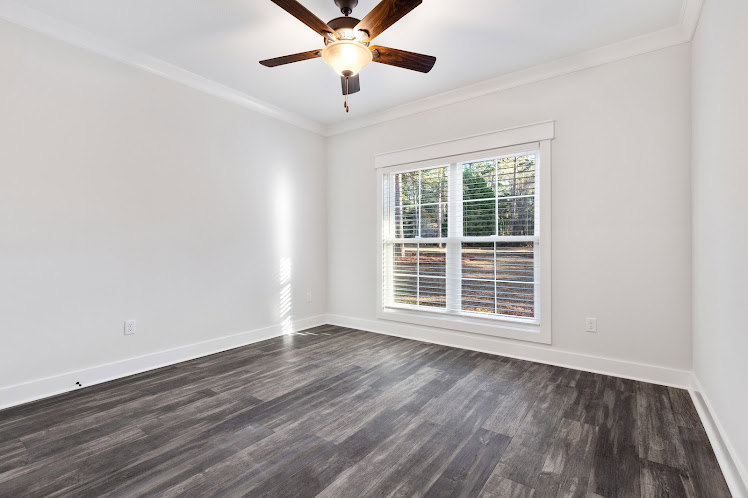 Bright room with white plaster walls, wood laminate flooring, ceiling fan, large window, and crown molding.