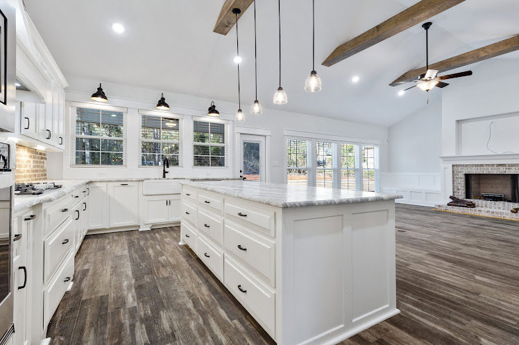 White kitchen with shaker cabinets, wood plank flooring, central island with drawers, quartz countertops, stainless steel appliances, and recessed lighting.