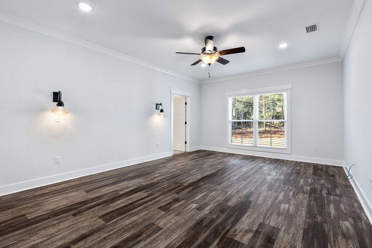 Wood flooring and plaster walls beneath a ceiling fan with light fixture in a bright residential room.