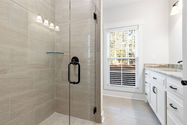 Modern bathroom featuring a frameless glass shower enclosure, white tile walls, light wood vanity with stone countertop, undermount sink, chrome faucet, and neutral tile flooring
