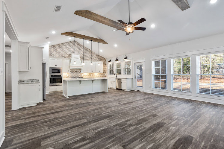 Spacious white kitchen featuring hardwood floors, white cabinetry, stainless steel appliances, and a ceiling fan above the central island