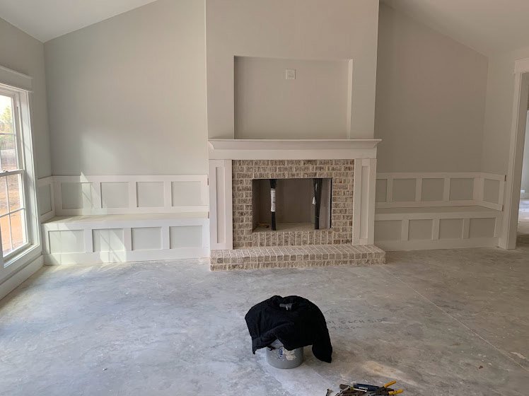Brick fireplace with white framed window, white bench featuring square panels and shelf, grey bucket with black jacket on wood floor