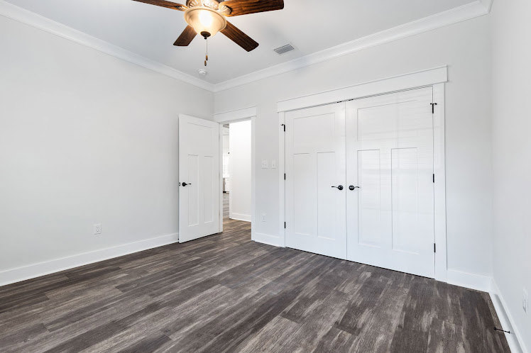 Room with white paneled doors, wood flooring, plaster walls, and a ceiling fan with light fixture