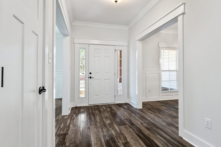 White room featuring smooth wood flooring, crisp white walls, and a simple doorway leading to an adjacent space.