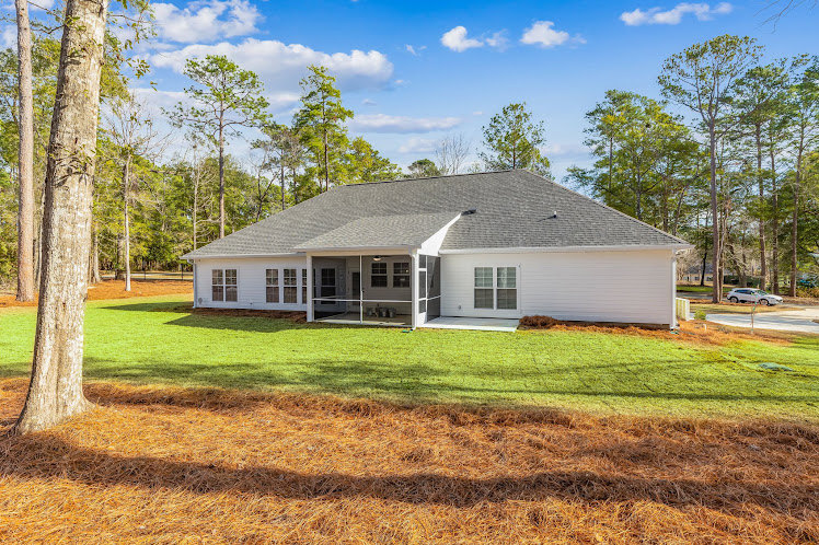 Two-story custom home with light siding, large windows, covered front porch, manicured green lawn, mature trees in the background, partly cloudy sky overhead