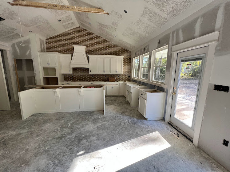 White kitchen with shaker cabinets, drawers, open shelving, exposed red brick walls, stainless steel sink, light wood flooring, and plaster ceiling.