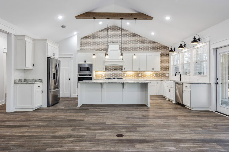Kitchen with exposed brick walls, wood flooring, row of wall-mounted lights, cabinetry, countertops, and a round object on the floor