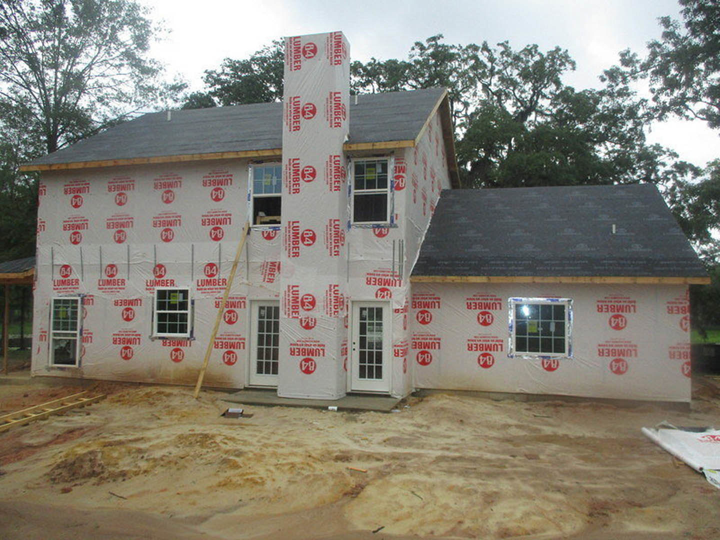 Two-story cottage with brick chimney, white siding, multiple-pane windows, white front door, and dirt yard; ladder leaning against exterior wall.