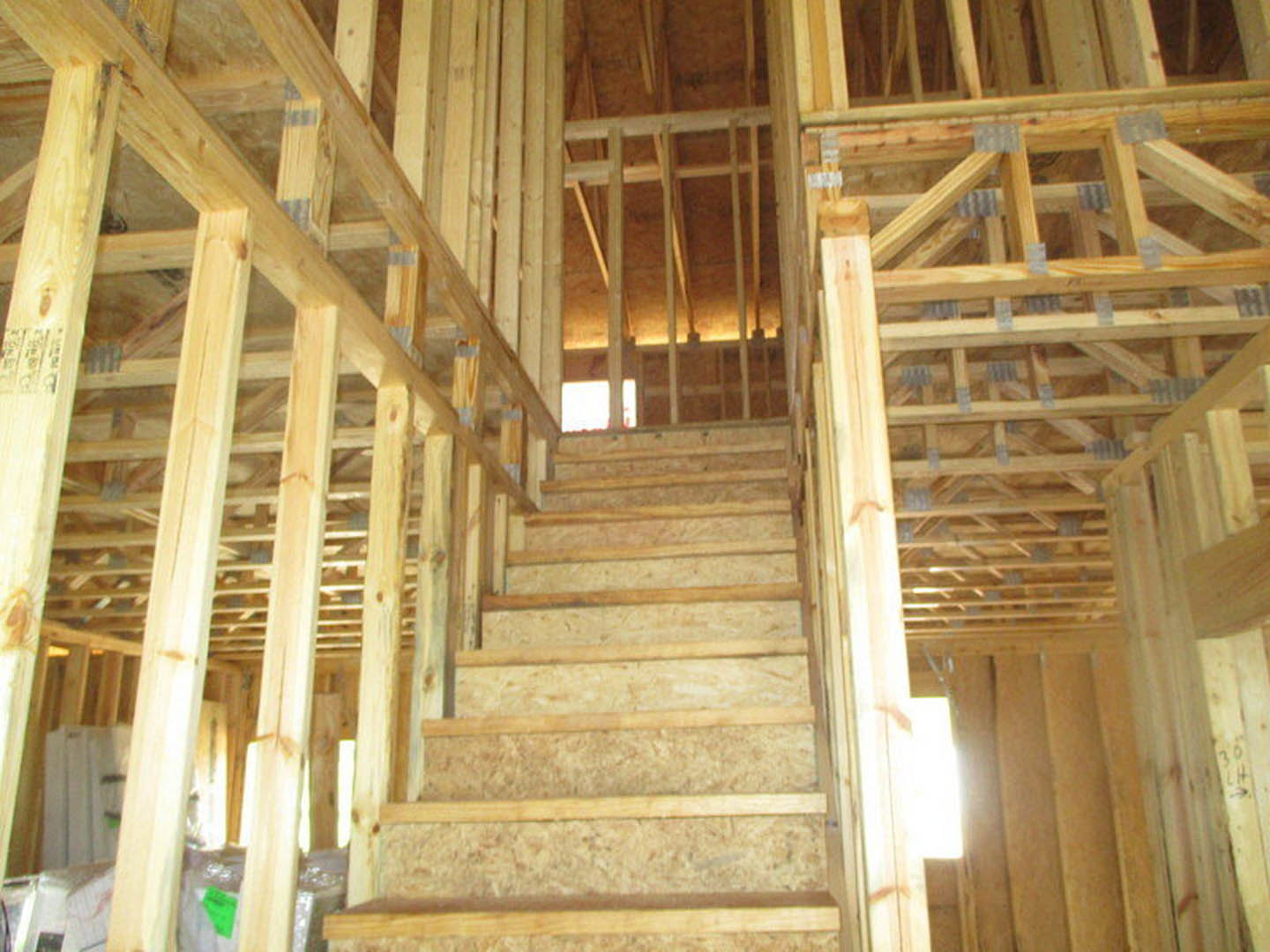 Hardwood staircase with wooden railing and exposed beams, sunlight streaming through window onto plank flooring, unfinished walls with visible insulation