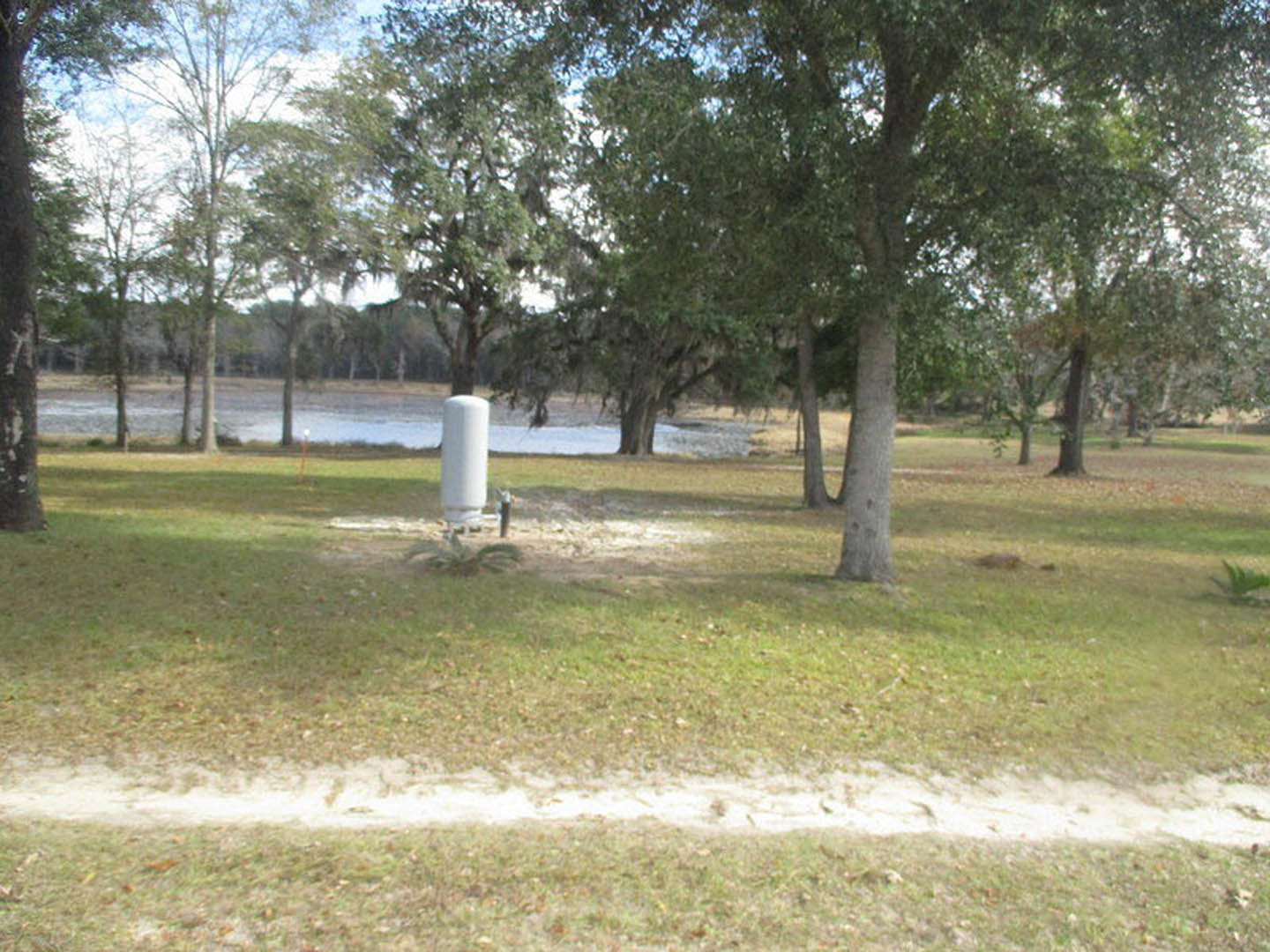 White water pump on grassy park field, surrounded by trees under clear blue sky
