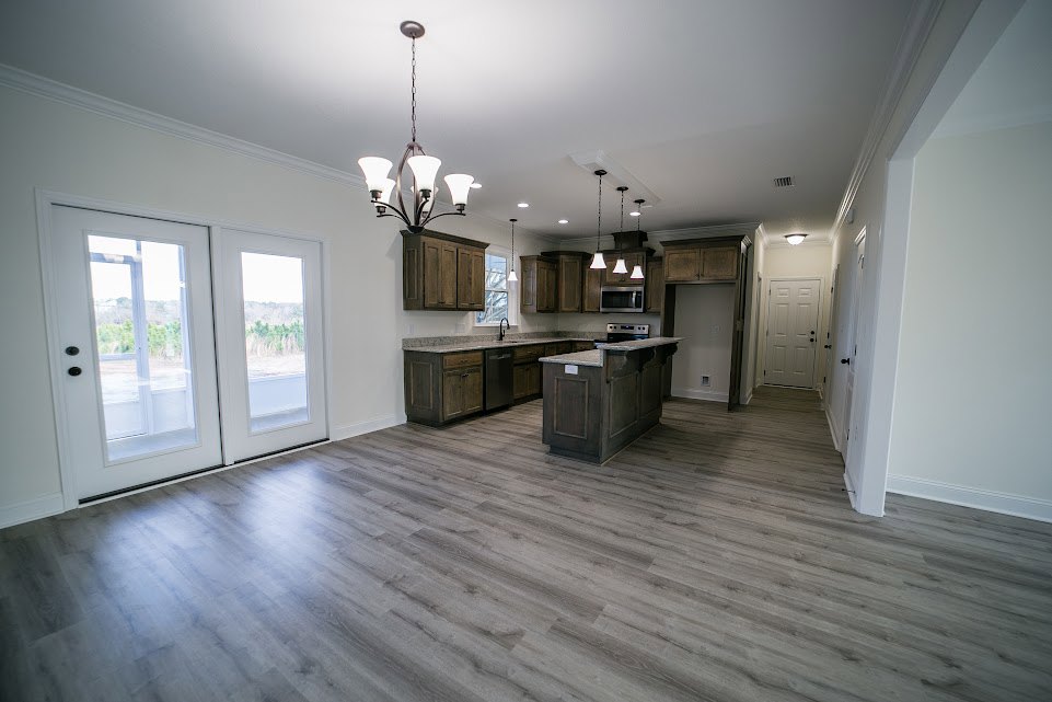 Open kitchen and dining area with wood flooring, white cabinetry, stone countertop, double glass doors, and white doors with black hardware