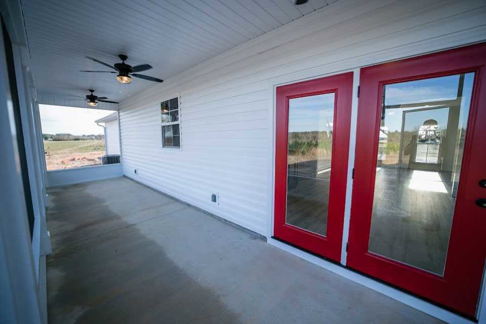 Red double doors with glass windows set in a white exterior wall, ceiling fan with light overhead, windows reflecting a road and illuminated from inside, red door adjacent to white