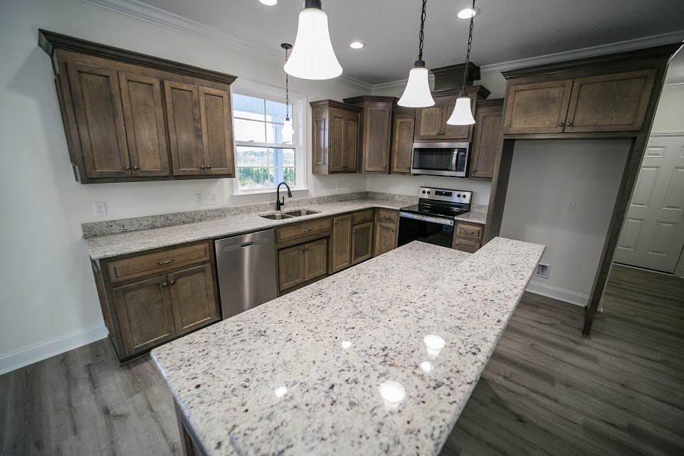 Marble kitchen countertop with stainless steel dishwasher, stove with handle, built-in microwave, white cabinetry, and pendant ceiling lights