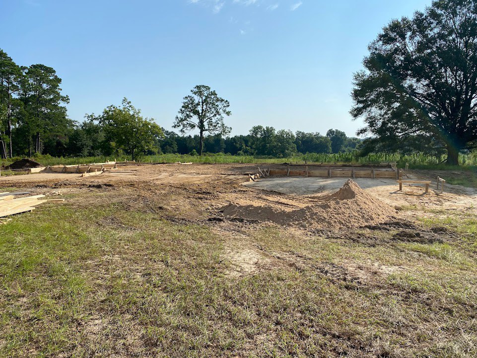 Dirt lot with a large tree and a pile of soil under a partly cloudy blue sky