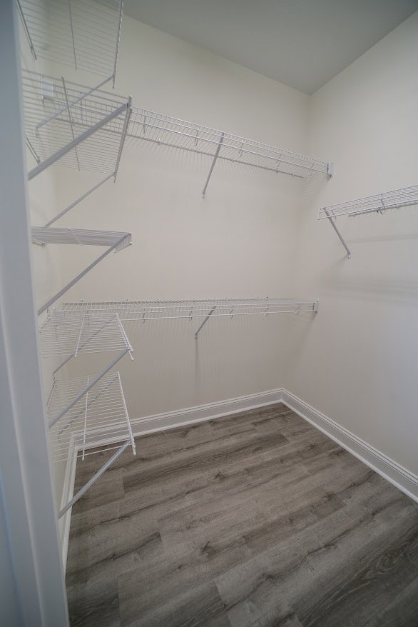 White built-in shelves mounted on a plaster wall, wood flooring with white base trim, white ceiling with exposed metal rods, minimalist interior.