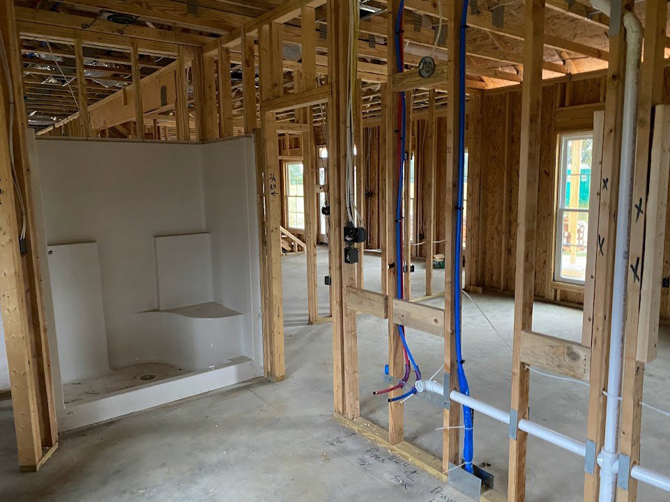 Bathroom under construction with exposed wooden framing, insulation, and unfinished walls; window overlooks blue and green outdoor scenery.