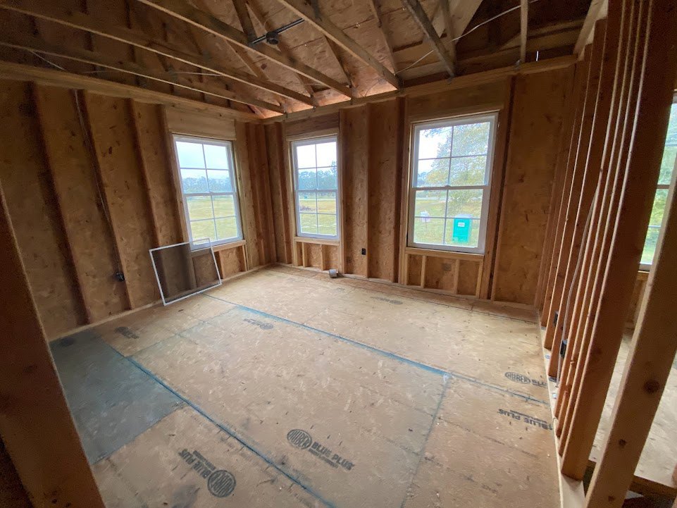 Room under construction featuring wood plank walls, exposed beams, tile flooring, and multiple windows overlooking trees and a field