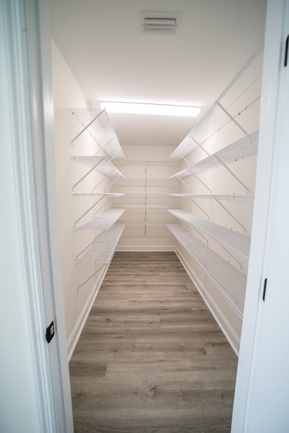 Hallway with built-in white shelves, wood flooring, white plaster walls, and a close-up of a vent and door.