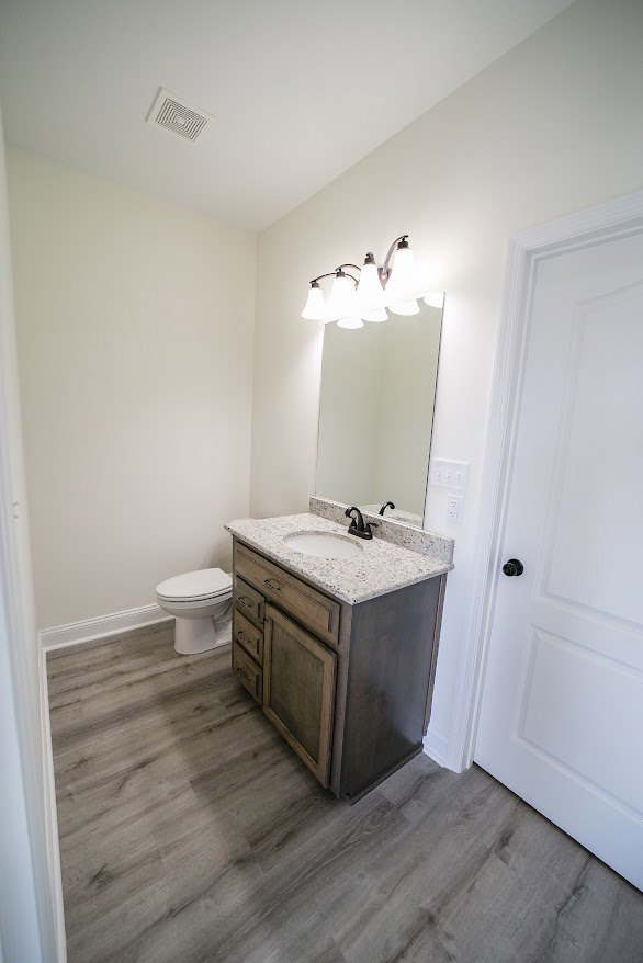 Modern bathroom with white toilet, rectangular sink featuring a black faucet, large wall mirror, light-colored tile flooring, and wood cabinetry with drawers.