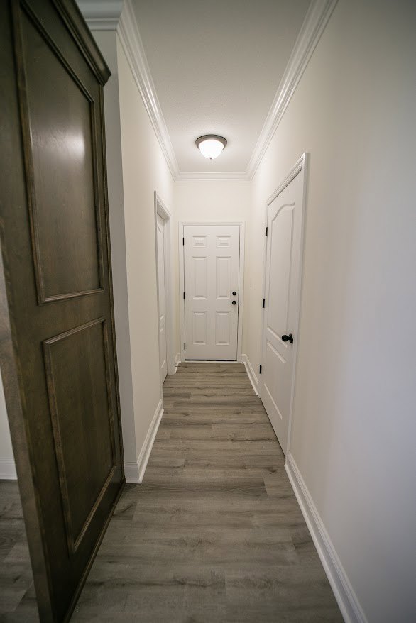 Hallway with white paneled doors featuring black hardware, wood plank flooring, white walls, and a ceiling-mounted light fixture