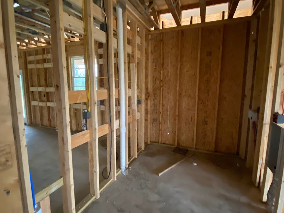 Open room with exposed wood beams, concrete floor, large window, black accent wall with white trim, and wood paneling.