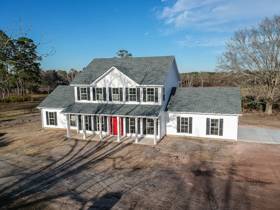 White siding house with multiple-paned windows, prominent red front door, leafless tree in front yard, cloudy sky overhead