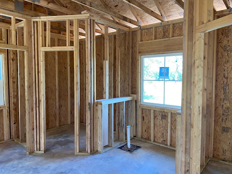 Unfinished room with exposed wood framing, two windows, building insulation, and concrete floor with wooden pallets