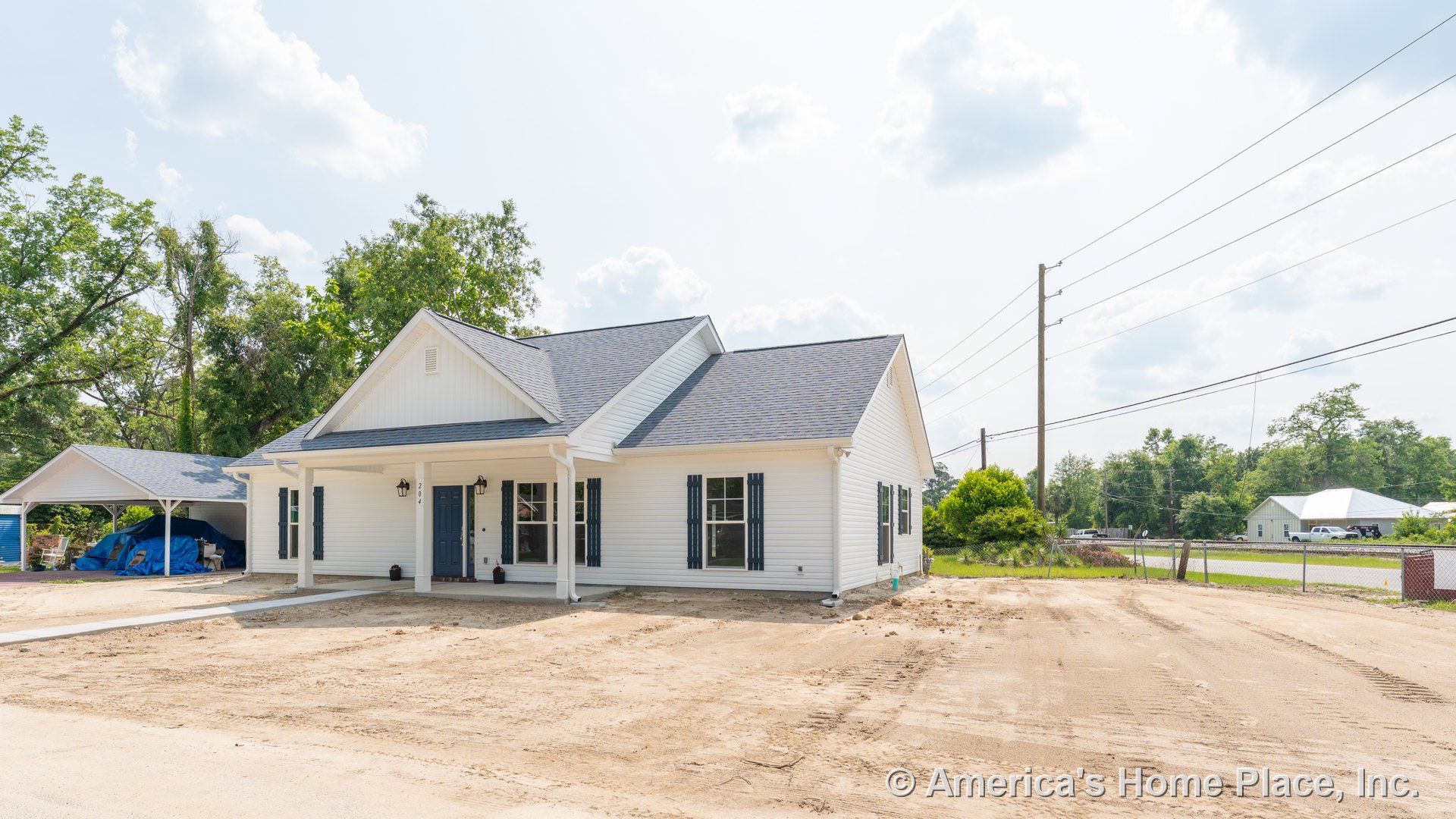 Covered front porch with white horizontal siding, dark window shutters, gable roof, double front windows, attached carport, entry door, decorative columns, exterior lighting, and